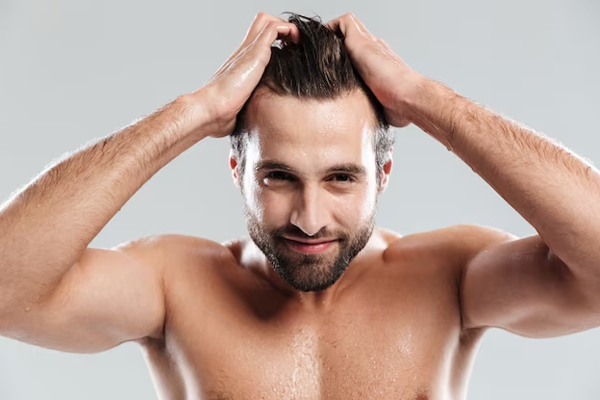 Caballero posando mientras toca su cabello, el cual se encuentra sano gracias a los cuidados capilares adecuados