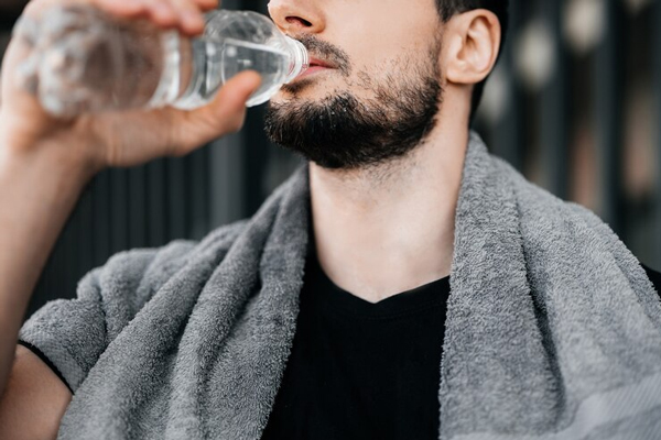 Fumar aumenta la caída del pelo - hombre joven con una toalla en el cuello bebiéndose una botella de agua