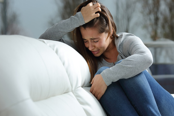 Salud mental - mujer sentada en el sofá en posición fetal agarrándose el cabello mientras llora