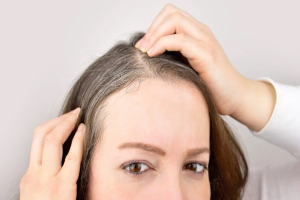 Cómo envejece nuestro pelo - Mujer tocándose el cabello canoso por el paso de los años y la falta de una rutina capilar adecuada