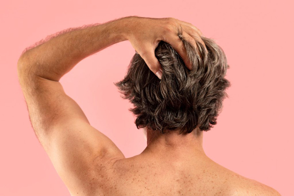 Cómo envejece nuestro pelo - Hombre de espalda tocándose con las manos el cabello que comienza a presentar canas a causa del envejecimiento prematuro del pelo