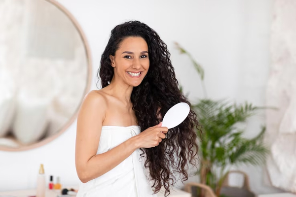 alopecia por tracción - mujer en su dormitorio tras el baño peinando su cabello rizado