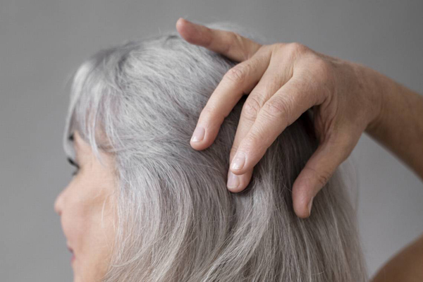 Cómo envejece nuestro pelo - Mujer tocándose con las manos el cabello con canas y seco debido al paso de los años