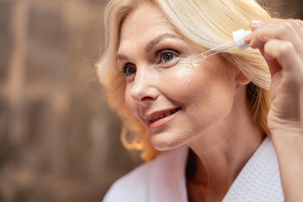Mujer mayor aplicando un serum en las líneas de expresión de sus ojos y pómulos