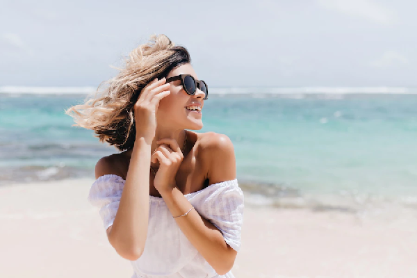 Revitalizar el pelo después del verano - Mujer de cabello corto disfruta del sol y la playa con gafas de sol 