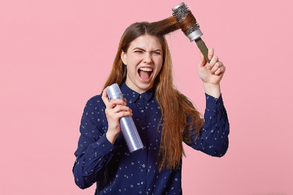Champús para crecer el pelo - Mujer de cabello marrón enreda un mechón de pelo en cepillo de metal para darle forma a sus puntas con laca