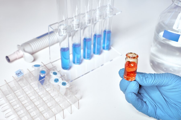 células madres - mesa de laboratorio con instrumental vario y la mano de un técnico con un vial de un compuesto naranja