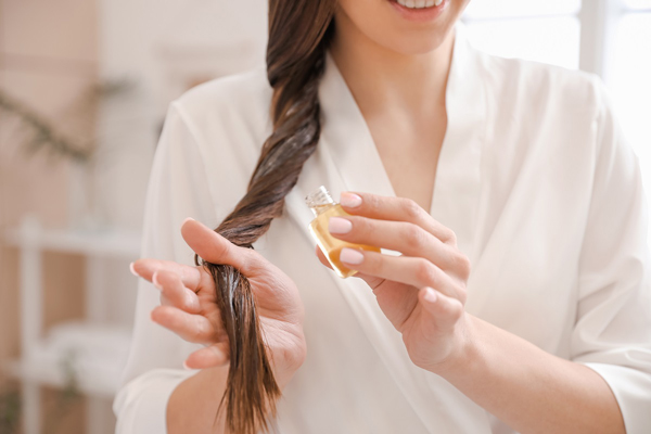 Nutrición para el pelo - Mujer aplica aceite esencial para contrarrestar la resequedad del cabello y mejorar la apariencia de las puntas 
