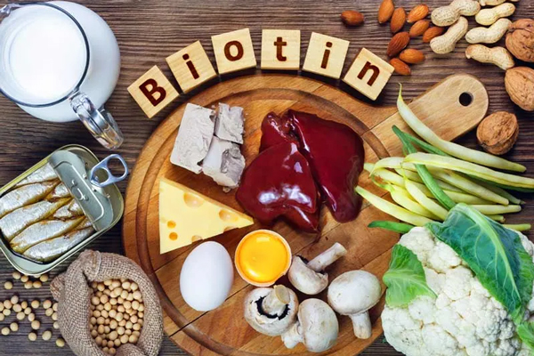 Biotina - Sardinas, hígado de res, queso, huevos y otros alimentos ricos en vitamina B7 presentados sobre una tabla de madera