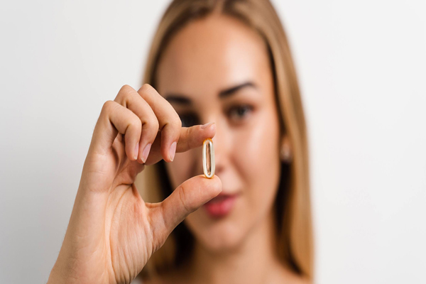 Biotina - Mujer de cabello claro sostiene cápsula de vitamina para el hacer crecer el pelo