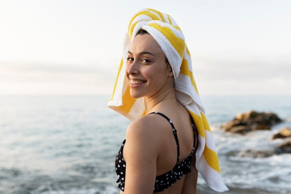 Revitalizar el pelo después del verano - Chica en bikini envuelve su cabellera en una toalla después de salir del mar 