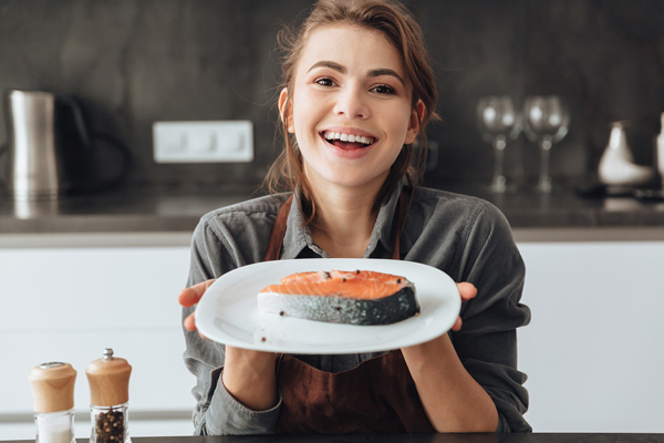 Mujer feliz sosteniendo un plato con un filet de salmón, el cual posee muchas vitaminas y minerales que mejoran la salud capilar