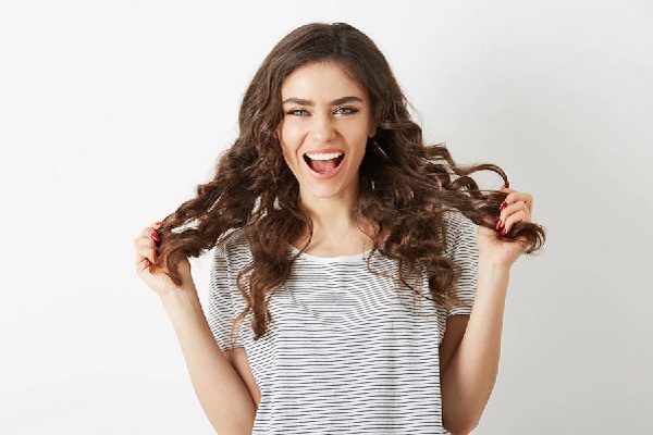 Cuidar el pelo en las mujeres - Mujer feliz sosteniendo su cabello ondulado, el cual se encuentra hidratado gracias a los cuidados capilares adecuados