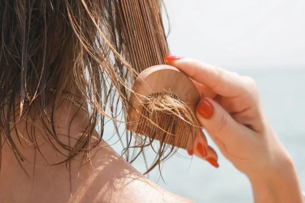 Revitalizar el pelo después del verano - Mujer cepilla su cabello con un peine de madera después de salir de la playa 