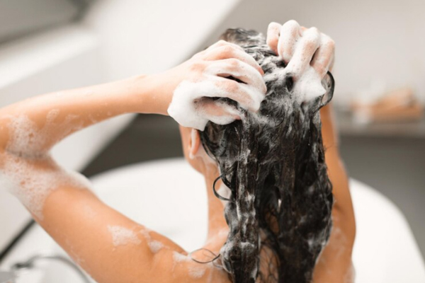 Champús para crecer el pelo - Joven aplica champú sobre su cabello para optimizar la limpieza de su cuero cabelludo en la ducha