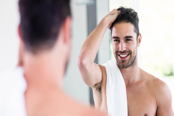 Nutrición para el pelo - Hombre peina su cabello con la mano mientras se mira frente al espejo 