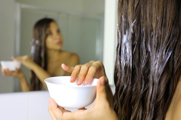 Mujer aplica mascarilla capilar para hidratar y regenerar su melena después de la playa 