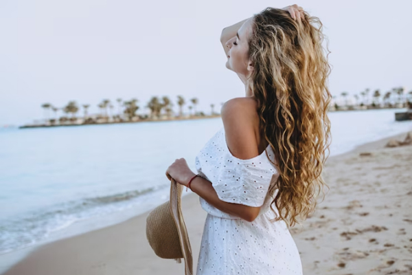 Revitalizar el pelo después del verano - Mujer de cabello rubio y rizado disfruta de la brisa del mar en su rostro 