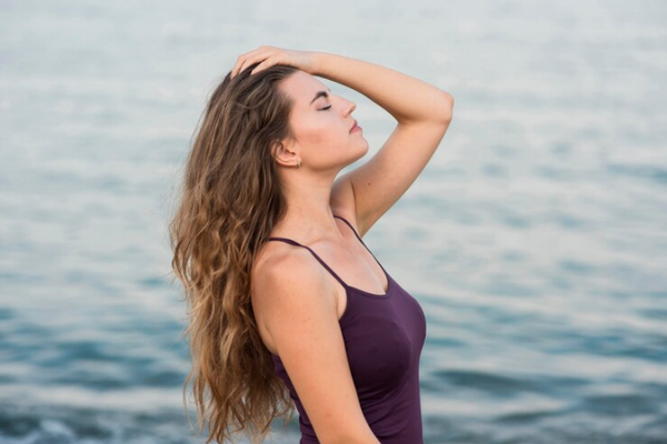 Joven en camiseta lleva su cabello castaño hacia atrás mientras disfruta del mar 