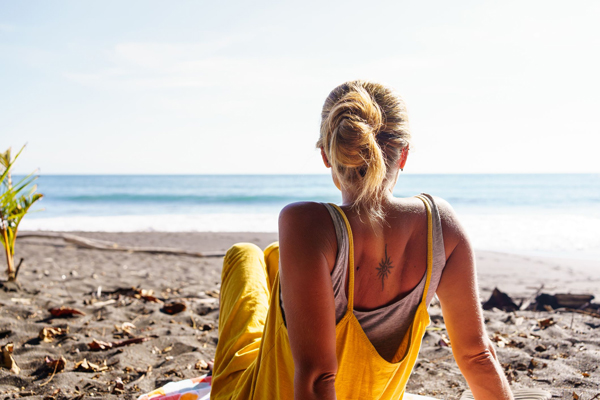 Revitalizar el pelo después del verano - Mujer se sienta a tomar el sol en la arena con el cabello recogido