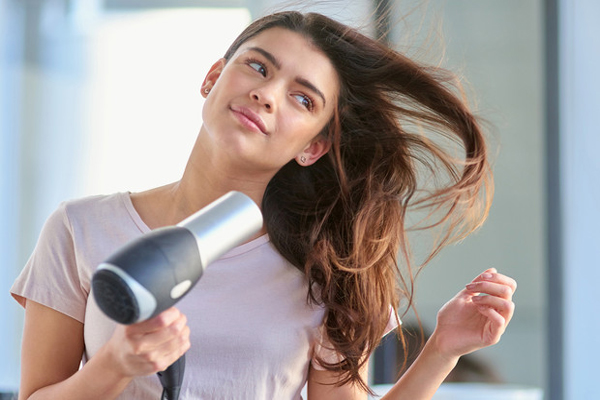 Chica secando su cabello con un secador eléctrico, para dar volumen al cabello y eliminar el exceso de humedad