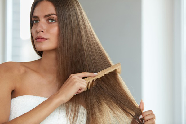 Keratina - Mujer de ojos claros cepilla su cabellera castaño claro con un peine de madera 