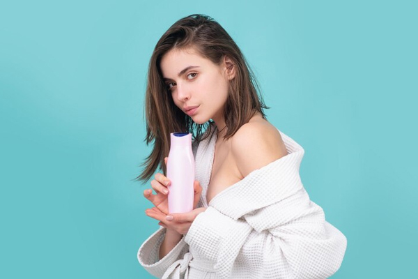 Chica en bata de baño presenta un excelente champú libre de sulfatos y parabenos