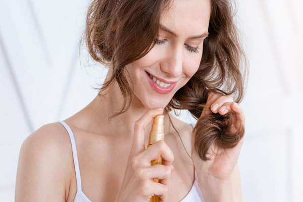 Aceite de argán - Mujer con cabello áspero y reseco se aplica un serum capilar en las puntas para mejorar su apariencia