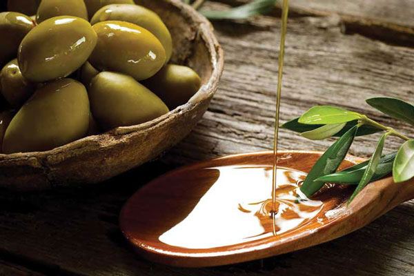 Aceite de oliva - Destilado de sustancia oleosa sobre una cuchara de madera junto a un tazón de aceitunas frescas 