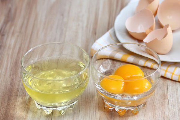 Yema y clara de huevo separadas en dos frascos de vidrio para elaborar una nutritiva mascarilla capilar 