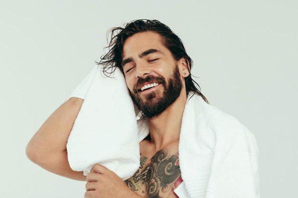 Hombre de hermosa sonrisa seca su abundante cabellera con una toalla de microfibra tras salir del baño