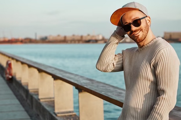 Hombre con gafas protege su cuero cabelludo con una gorra mientras disfruta de un atardecer en el muelle