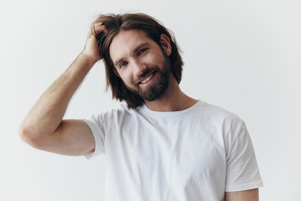 Tips para hacer crecer el pelo - Hombre con barba peina su abundante cabellera con la mano