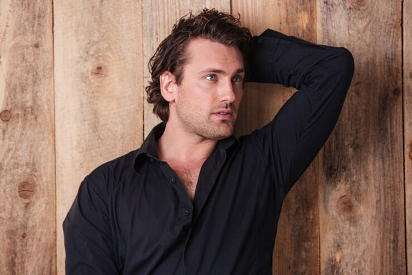 Cortes de pelo largo para hombre - Chico rubio de camisa negra peina su cabello con las manos para verse más sexy ante las chicas