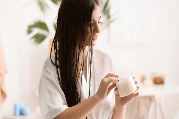 Mujer con mascarilla capilar en mano se prepara para brindarle una dosis extra de hidratación al pelo