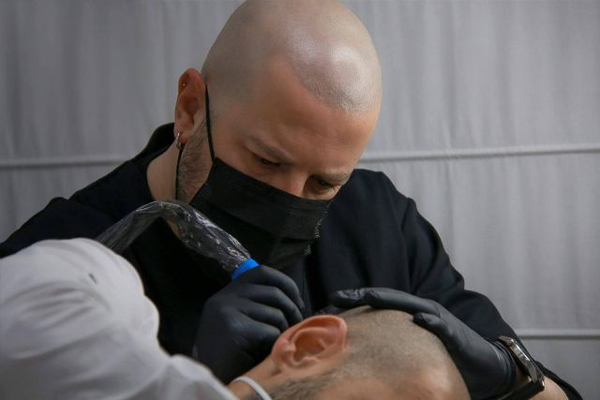 Especialista en tatuajes capilares lleva a cabo una sesión para refrescar la imagen de un cliente