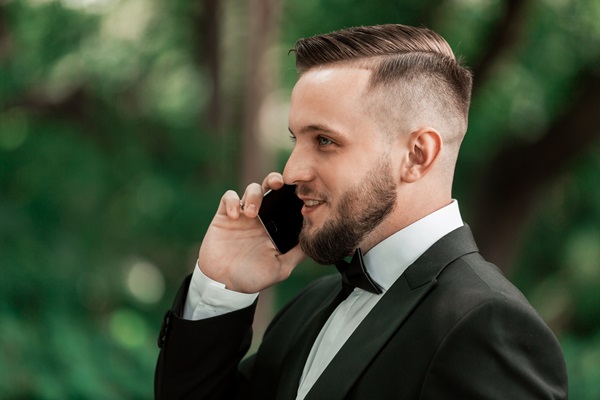 Peinados de hombre para bodas - Hombre conversando por su teléfono el día de la boda, con un peinado de raya lateral, el cual lo hace ver elegante y formal