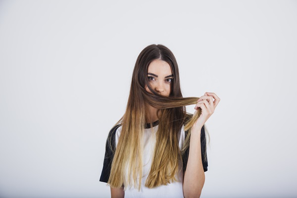 Mujer sosteniendo y oliendo su cabello, el cual ha perdido vida por el uso de productos químicos para teñirlo