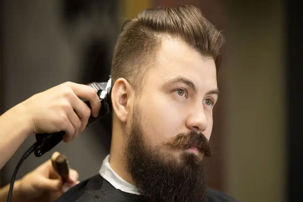 Hombres con entradas - Hombre de cara redonda se mira frente al espejo mientras el barbero termina de pulir su corte