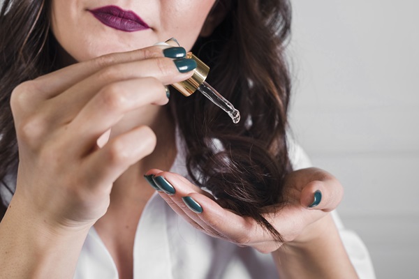 Aceite de ricino para el pelo - Mujer aplicando unas gotas de aceite de ricino en el cabello, para fortalecerlo y acelerar el crecimiento