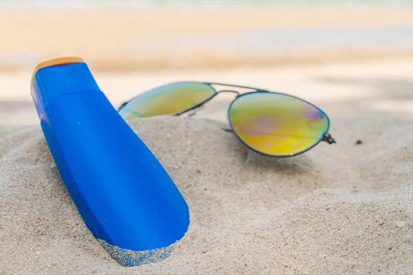 Protector solar - Imagen de un protector solar para el cabello y uno lentes, colocados sobre la arena de la playa
