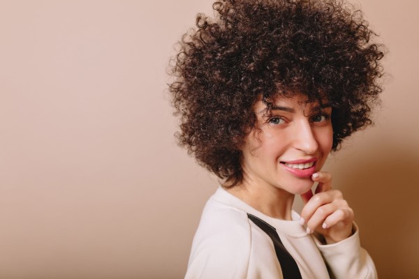  Amable mujer linda con rizos y maquillaje desnudo sonríe a la cámara y disfruta de buen humor