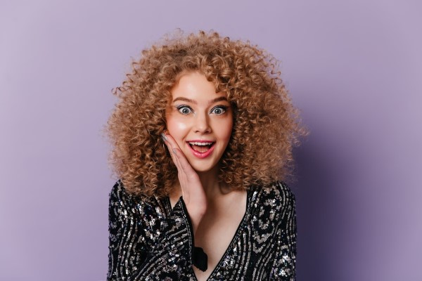 densidad del cabello rizado - mujer con el cabello rizado alegre y cara de sorpresa con un vestido elegante en blanco y negro