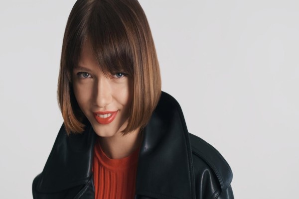  Hermosa modelo de moda con cabello bob y labios rojos mirando con confianza a la cámara y sonriendo sobre fondo blanco