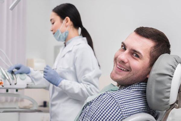 Caries y calvicie - Paciente de buen ánimo espera a que su dentista termine de alistar sus herramientas para hacerle una revisión exhaustiva 