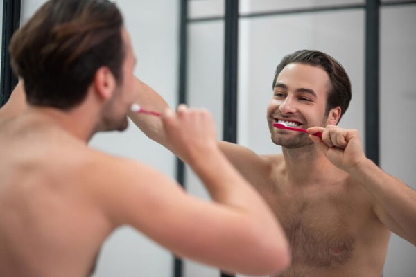 Joven atractivo se cepilla frente al espejo para preservar el blanco de sus dientes 