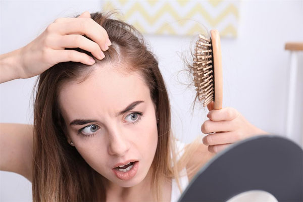 Joven se mira impactada frente al espejo tras experimentar una significativa caída del cabello 
