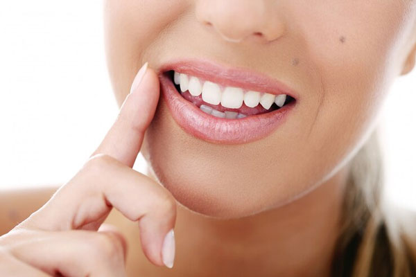 Caries y calvicie - Mujer de bella sonrisa señala su boca para exaltar el blanco de sus dientes 