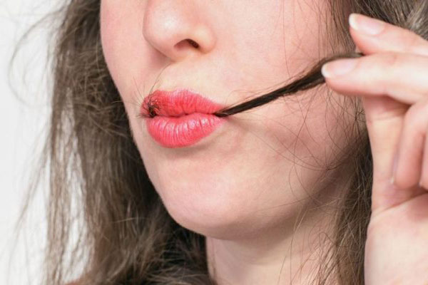 Tricofagia - Joven de labios rojos visiblemente angustiada se lleva un mechón de cabello a la boca 