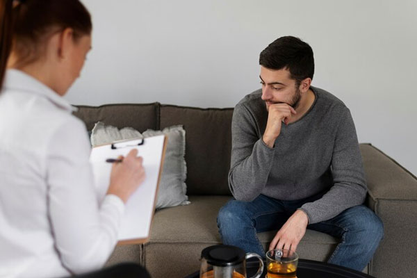 Hombre mira hacia el suelo mientras la terapeuta toma nota de los orígenes de su conducta